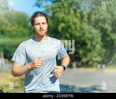 Junger, sportlicher Mann, der am Sommertag im grünen Park im Freien läuft Stockfoto