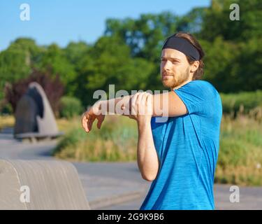 Junger gutaussehender Athlet, der sich vor dem morgendlichen Training im grünen Park aufwärmt Stockfoto