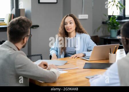 Junge Geschäftsfrau, die während eines Gesprächs bei einem Arbeitsgespräch einen männlichen Kollegen ansieht Stockfoto