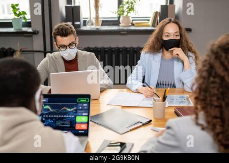 Gruppe junger interkultureller Manager in Schutzmasken, die im Büro arbeiten Stockfoto