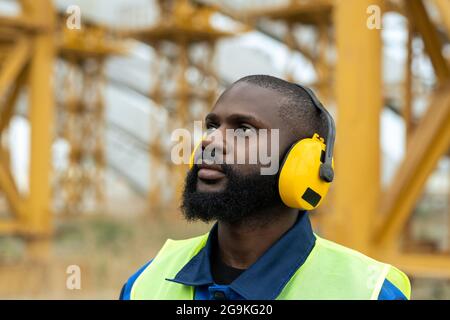 Afrikanischer bärtiger Ingenieur mit Kopfhörern, der draußen auf der Baustelle arbeitet Stockfoto