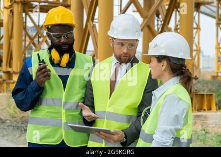 Zwei Ingenieure nutzen digitale Tablets und diskutieren gemeinsam mit Bauarbeitern im Freien über das Projekt Stockfoto