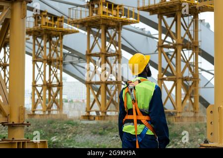 Rückansicht des Bauarbeiters in der Ausrüstung, der durch die Baustelle läuft und Gebäude betrachtet Stockfoto