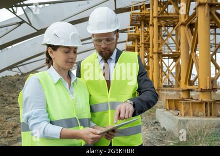 Zwei Ingenieure in reflektierender Kleidung, die auf der Baustelle auf einem digitalen Tablet arbeiten Stockfoto