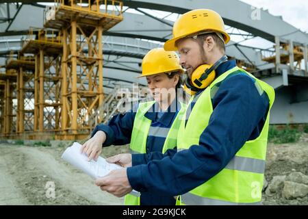 Zwei Arbeiter in Arbeit Helme untersuchen Blaupause während ihrer Arbeit auf der Baustelle Stockfoto
