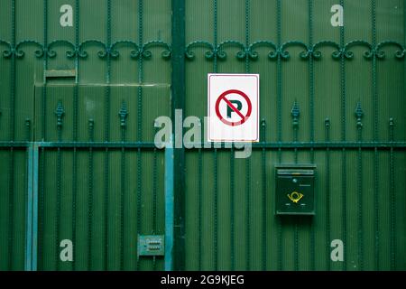 Grünes Metall, moderner Garageneingang. Ein rot-weißes No Parking-Schild, das an einem Sicherheitszaun aus Metall befestigt ist. Ein Briefkasten auf schmiedeeisernen Toren. Bitte Stockfoto