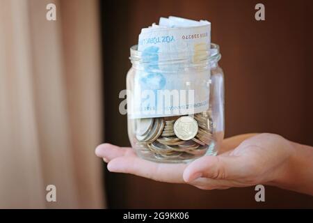 Türkische Lira-Banknoten und Münzen im Glasglas, Frauenhand. Die Papierwährung der Türkei. Die aktuellen türkischen Lira werden von der Zentralbank der Re ausgegeben Stockfoto
