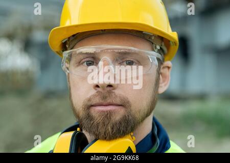 Nahaufnahme eines Bauarbeiters in einem Arbeitshelm und einer Schutzbrille, der die Kamera anschaut Stockfoto