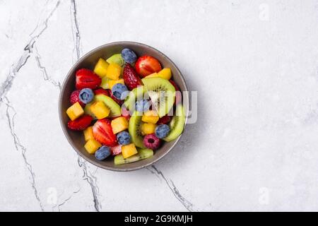 Natürliche Bio-Lebensmittel für ein gesundes und ernährungsförderliches Leben. Blick von oben auf frischen Obstsalat mit Kiwi, Erdbeere, Heidelbeere, Himbeere und Pfirsich auf weißem Marmor Stockfoto