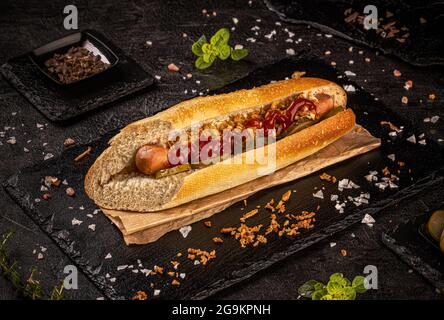 Köstlicher Hot Dog mit Gurken, getrockneten Zwiebeln und Ketchup auf schwarzem Schiefergrund, Stillleben Stockfoto