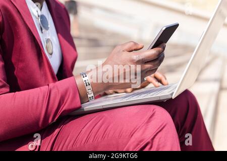 Detail der Hand eines afrikanischen Geschäftsmannes mit einem Smartphone und Computer-Laptop, Technologie und Remote-Work-Konzept Stockfoto