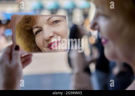 Ziemlich ältere weiße Frau schaut im Spiegel draußen. Stockfoto
