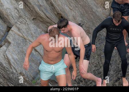 Eine Gruppe junger männlicher Urlauber klettert in Towan Head in Newquay in Cornwall über Felsen. Stockfoto