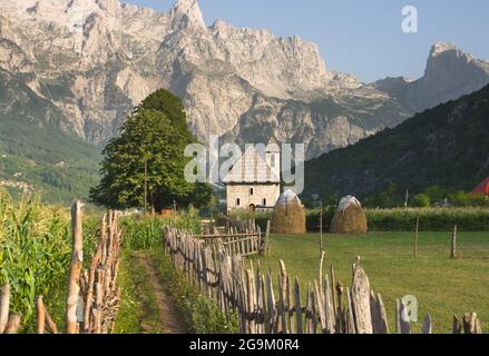 Ein Weg mit Holzzaun führt die katholische Kirche im Theth-Tal, im Hintergrund die Berge der albanischen Alpen Stockfoto