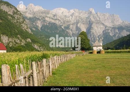 Holzzaun führt die katholische Kirche im Theth-Tal, im Hintergrund die Berge der albanischen Alpen Stockfoto