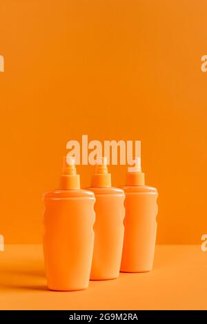 Sprühflaschen mit Sonnenschutzmitteln, isoliert auf Orange Stockfoto