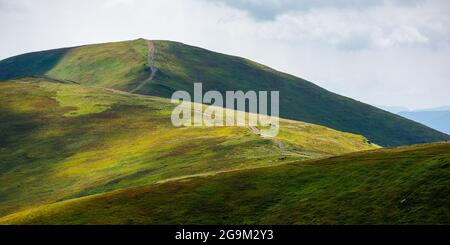 Sanfte Hügel der borzhava Berge. Weg durch die Spitze des Grats. Schöne Naturlandschaft mit grasbewachsenen Hängen in getupftem Licht. Wunderbarer Sommer Stockfoto