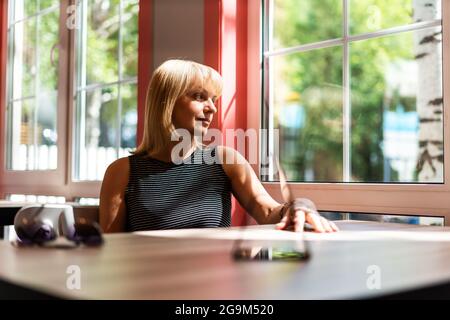 Nachdenkliche Erwachsene reife Frau, die durch das Fenster schaut, während sie am Tisch im Café sitzt. Frau mittleren Alters entspannend. Stockfoto