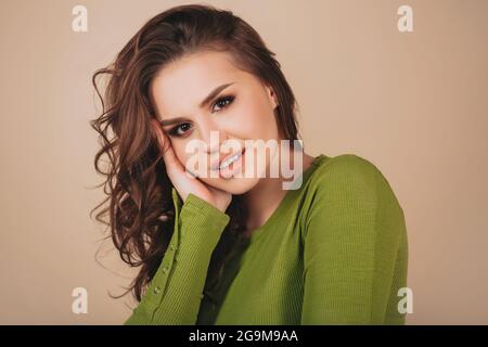 Nahaufnahme Porträt einer jungen nachdenklichen Brünette Frau mit ernstem Gesichtsausdruck, die seitwärts steht und in einem leuchtend grünen Hemd direkt auf die Kamera schaut Stockfoto