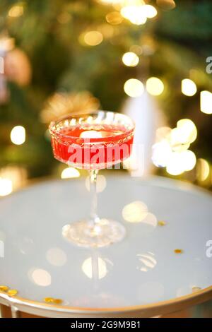 Vertikale Aufnahme eines klassischen kosmopolitischen Cocktails in Glas, der im Nachtclub oder Restaurant über verschwommene festliche Lichter steht und funkelt. Modern Stockfoto