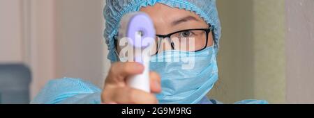 Banner mit Krankenschwester oder Arzt im medizinischen Einweganzug misst die Körpertemperatur des Patienten mit einem medizinischen Infrarot-Thermometer. Thermometerpistole Isom Stockfoto