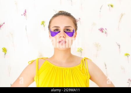 Positive junge Frau mit violetten Augenflecken, die während der Hautpflege mit einem Lächeln auf die Kamera blicken. Natürlichkeit und Öko-Konzept Stockfoto