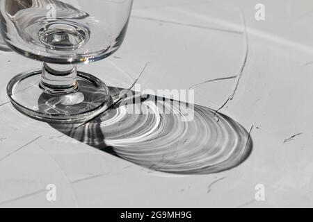 Glas auf einem grauen Betontisch mit Sonnenstrahlen und Reflexionen, Blick von oben, abstrakten Schatten und Sonnenlicht Stockfoto