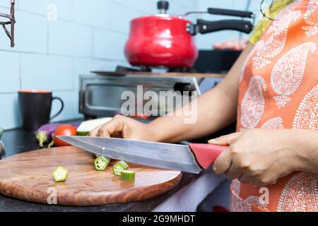 Nahaufnahme der indischen jungen Frau, die Schürze kocht und Gemüse in der heimischen Küche auf dem Gasherd schneidet Stockfoto