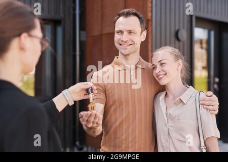 Weibliche Immobilienmaklerin, die Schlüssel für ein glückliches Paar im Freien gibt, Platz kopieren Stockfoto