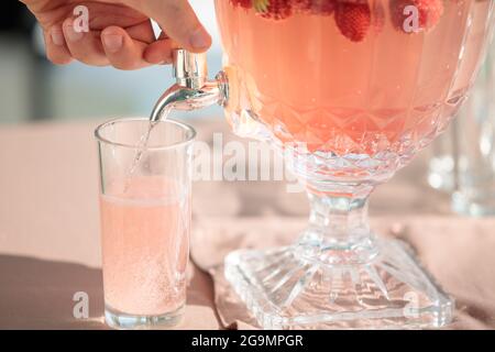 Limonade per Hand aus einer Dose mit einem Wasserhahn gießen, Erdbeeren schwimmt in einer transparenten Dose Stockfoto