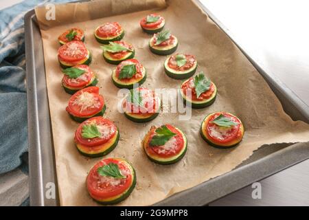 Mini Pizza Snack aus dem Ofen, hausgemachte aus Scheiben von Zucchini, Tomaten und Parmesan mit Petersilie garnieren auf einem Backblech, ausgewählte Fokus, schmal de Stockfoto