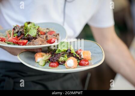 Der Kellner trägt Teller mit Salaten aus der Nähe Stockfoto