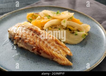 Sautierter Kabeljaufisch mit Fenchelgemüse und orangefarbenen Scheiben auf einem blauen Teller serviert, ausgewählter Fokus, enge Schärfentiefe Stockfoto