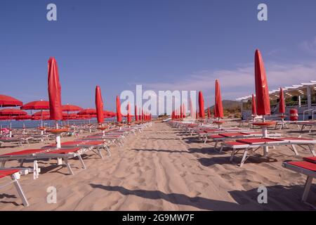 Rote Sonnenliegen und Sonnenschirme am Sandstrand am Meer. Leere Sonnenliegen am Meer. Stockfoto