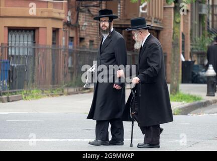 Ein junger orthodoxer jüdischer Mann hilft einem älteren Menschen, die Straße zu überqueren. Auf der Bedford Avenue in Brooklyn, New York City. Stockfoto