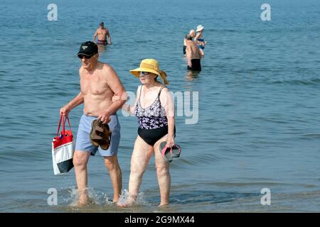 Ein älteres Paar, vermutlich Ehemann und Ehefrau, läuft Arm in Arm entlang der Küste am Brighton Beach in Brooklyn, New York. Sie halten ihre Sandalen Stockfoto