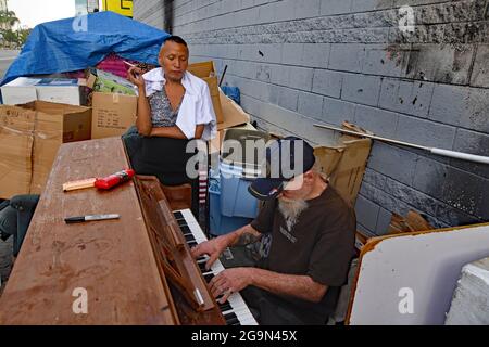 Skid Row, Downtown Central Los Angeles, Kalifornien, USA, Juni 2021. Nancy, eine Frau aus Missouri raucht CrystalMeth, während Rodney, ein Mann aus Ohio, der früher professioneller Musiker war, Spielt das Hotel California auf einem aufgelösten Klavier, das auf den Straßen gefunden wurde.Los Angeles steht vor einer humanitären Krise, die es noch nie zuvor gesehen hat, da Obdachlosigkeit und Drogenmissbrauch in der Gegend namens „Skid Row“ zunehmen. Die Covid-19-Pandemie hat das Problem noch verstärkt, da die Immobilienpreise durch das Dach gingen, die Arbeitslosenquote zunahm und die illegale Einwanderung eine Explosion in der Obdachlosigkeit verursachte. Schätzungsweise 70,000 Menschen durchstreifen die Stockfoto