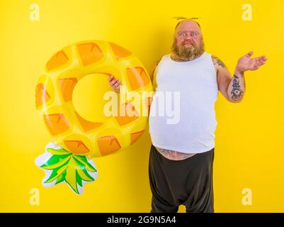 Ein fetter, nachdenklicher Mann mit Perücke im Kopf ist bereit, mit einem Donut-Lebensretter zu schwimmen Stockfoto