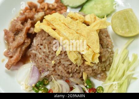 Reis gemischt mit Garnelenpaste Belag Scheibe Thai Ei Omelett paar süßes Schweinefleisch in Soße und Gemüse auf dem Teller Stockfoto
