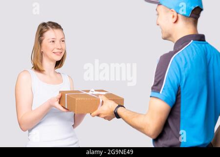 Zufriedene blonde Frau im weißen T-Shirt nimmt den Lieferkarton des Kuriermanns in Uniform. Stockfoto