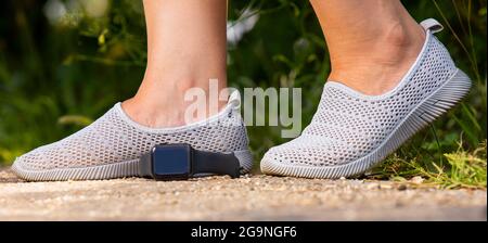 Nahaufnahme der Beine einer Frau in bequemen Schuhen zum Joggen im Freien und digitale Uhr liegt auf dem Boden. Stockfoto