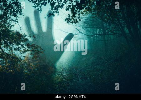 Ein Horrorkonzept einer geisterhaften Figur mit der Hand in der Luft. In einem dunklen, gespenstischen Wald. Mit einer Grunge, texturierten Bearbeitung Stockfoto