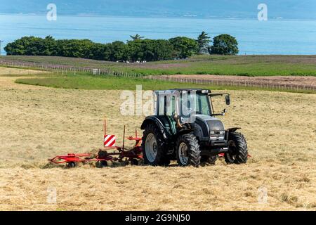 Traktor und Heubob drehen Heu in der Nähe von Portmahomack, Easter Ross, Schottland. Stockfoto