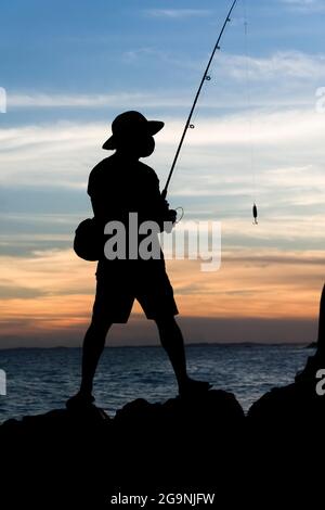 Salvador, Bahia, Brasilien - 25. April 2021:Silhouette der Fischer auf den Felsen des Rio Vermelho Strand in Salvador, Bahia, Angeln für ihre Lebensmittel und Stockfoto