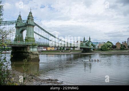 HAMMERSMITH LONDON 27 Juli 2021 . Ruderer passieren die Hammersmith Bridge in West London, die seit April 2019 für Kraftfahrzeuge und alle Nutzer im August 2020 für Radfahrer und Fußgänger wieder geöffnet ist. Hammersmith Bridge ist eine 253 m lange, 134 Jahre alte gusseiserne Hängebrücke, die letztes Jahr wegen Sicherheitskontrollen geschlossen wurde, nachdem Risse entdeckt wurden. Credit amer Ghazzal/Alamy Live News Stockfoto