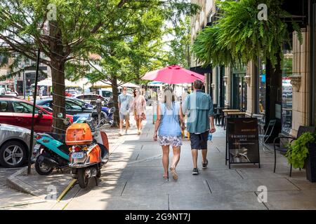 ASHEVILLE, NC, USA-22 JULY 2021: Ein Sommertag auf Page Ave. In der Innenstadt, zeigt zwei Paare, die vorbei gehen und zwei bunte Gasmotorroller geparkt Stockfoto