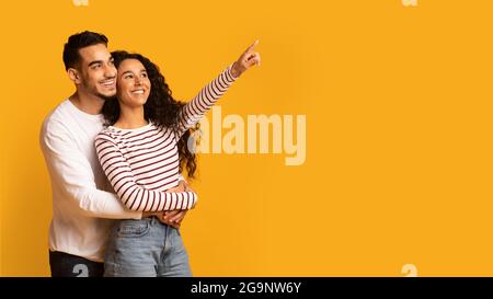 Fröhliches Junges Arabisches Paar, Das Mit Dem Finger Auf Copy Space Zeigt Stockfoto