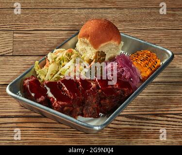 Gebackene Schweinelende mit Grillsauce und Gemüsegarnitur auf Kunststoffplatte Stockfoto