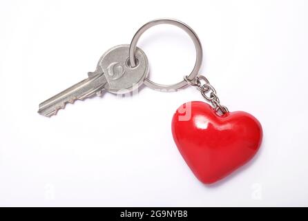 Hausschlüssel und roter herzförmiger Schlüsselanhänger auf weißem Hintergrund Stockfoto