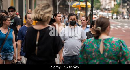 Sonntagnachmittag auf der 5th Avenue in New York City, 25/07/21. Nachdem die überfüllten Straßen New Yorks während der COVID-19-Pandemie still wurden, sind die Menschen wieder auf der Straße, viele sind ohne Maske oder Gesichtsbedeckung unterwegs. Das Foto zeigt einen Mann (rechts), der eine Gesichtsbedeckung trägt, während andere, die darauf warten, die 51. Straße auf der 5th Avenue zu überqueren, dies nicht tun. Stockfoto
